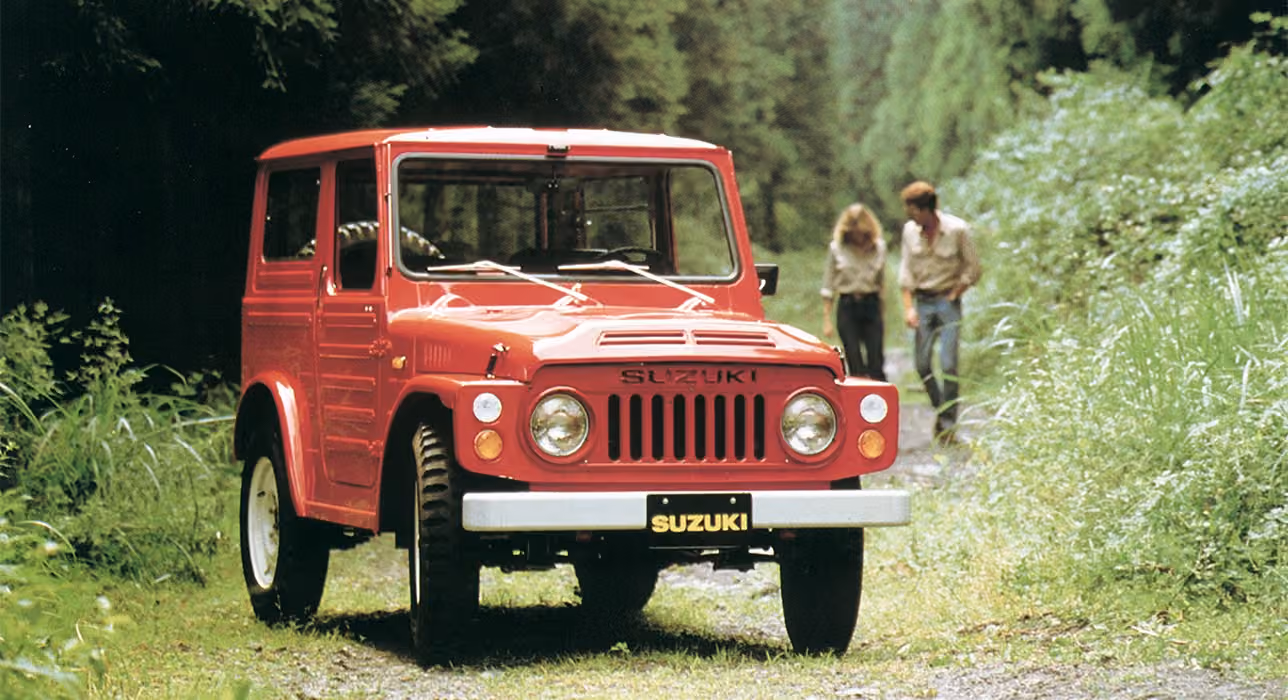 Abbildung zeigt einen roten Jimny parkend auf einem Waldweg