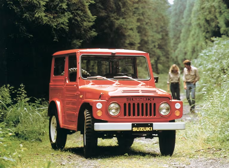 Abbildung zeigt einen roten Jimny parkend auf einem Waldweg