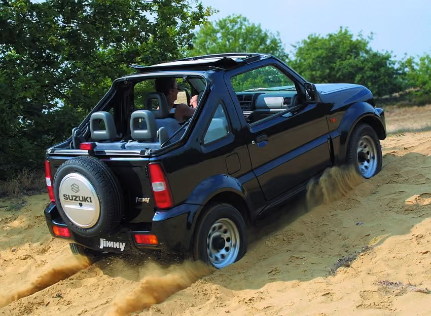 Abbildung zeigt einen schwarzen Jimny, der einen Sandhügel hinauffährt